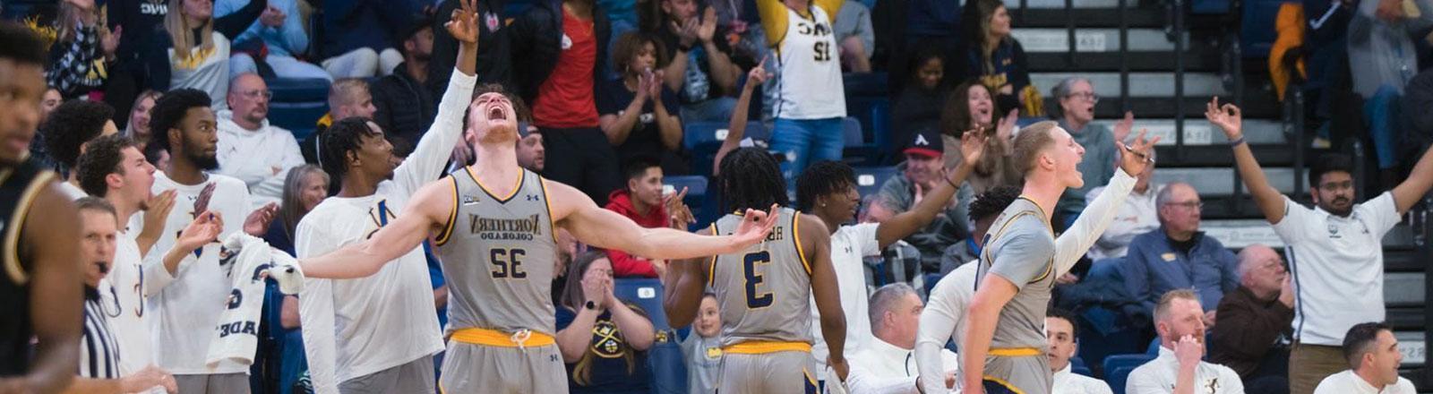 Men's basketball student-athletes on the bench celebrating